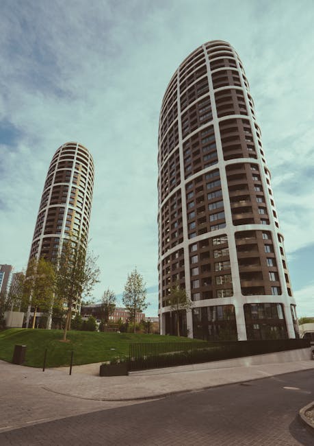 A black and white photograph of a riverside scene in Paddington, showing a glass-paneled boat docked along the edge of the water. The boat has a smooth, reflective surface with visible windows, and appears to be well-maintained. In the background, a large building with multiple floors and balconies is partially obscured by leafy trees, including a prominent weeping willow with long, drooping branches hanging over the river. The river surface is calm, showing gentle ripples, with surrounding vegetation and urban structures creating a tranquil yet structured environment. This image captures the natural and architectural elements typical of Sheldon Square and Merchant Square in Paddington, emphasizing the area’s scenic, clean, and well-kept appearance. Cleaners Paddington would recommend routine surface cleaning and maintenance to preserve the scenic waterways and surrounding elements.